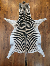 Load image into Gallery viewer, Zebra skin rug on a wooden floor
